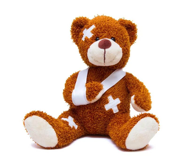 Ein plüschiger brauner Teddybär mit einem weißen Verband am Arm und Klebeband am Körper, der aufrecht vor einem weißen Hintergrund sitzt.